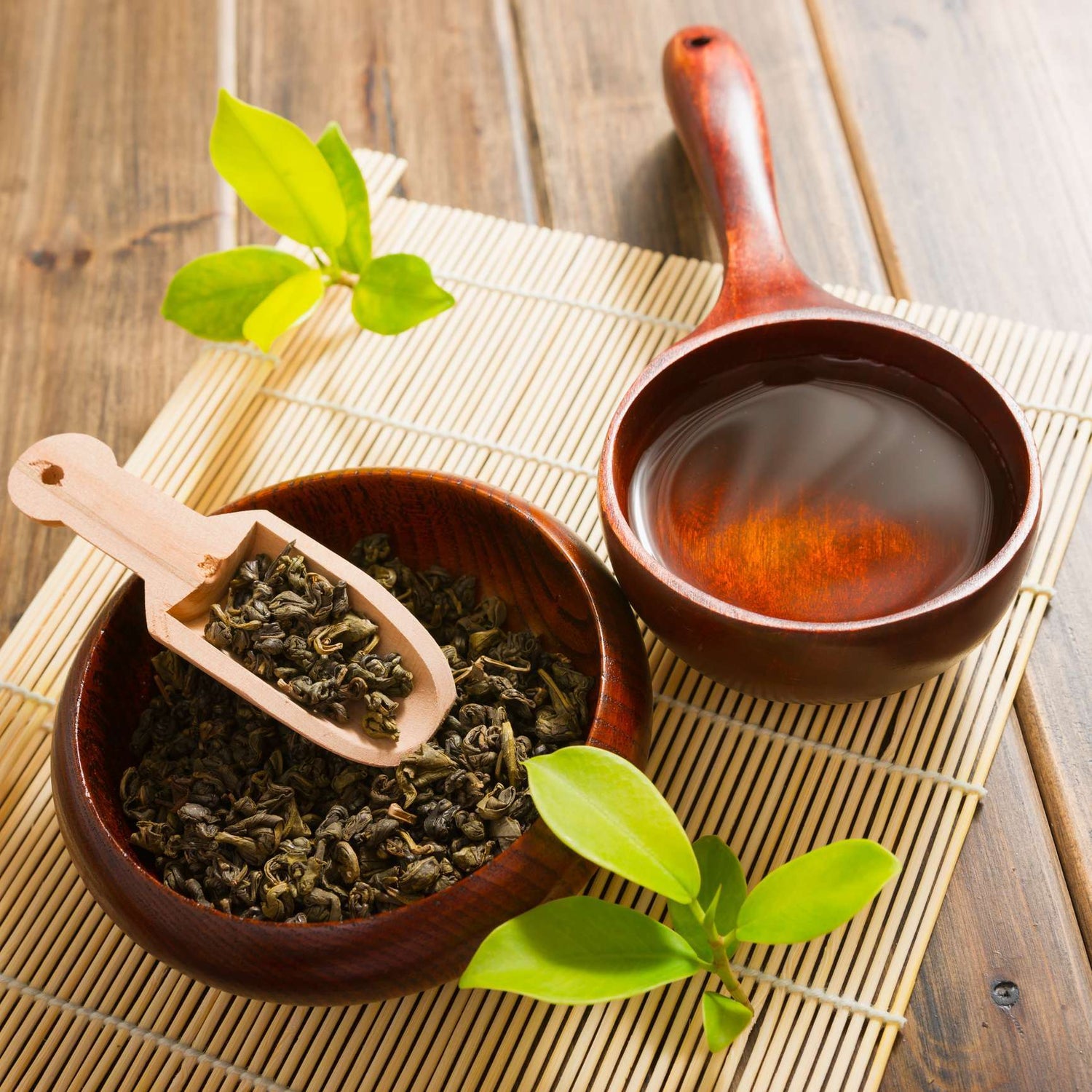 Foto schaaltjes op bamboe mat met thee en theebladeren met een schepje en groene blaadjes